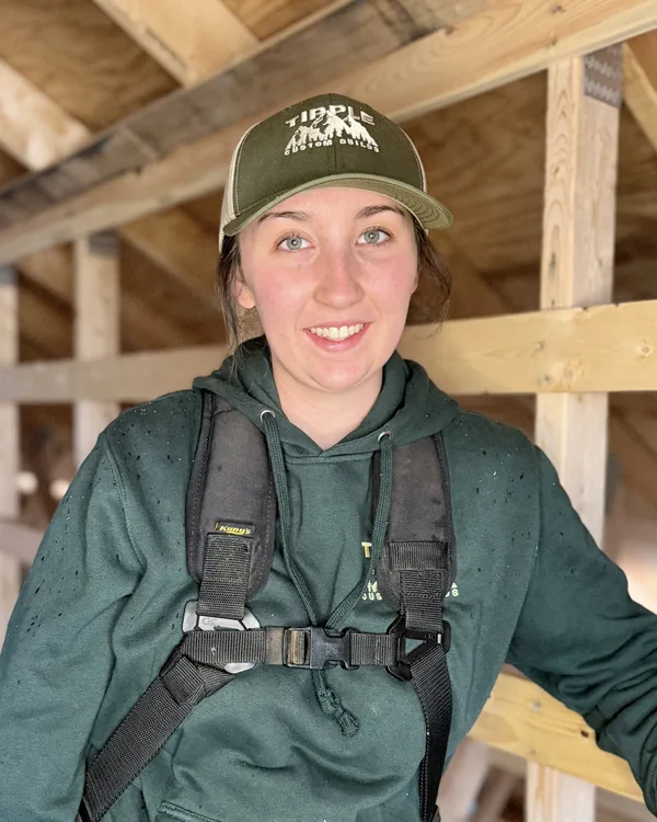 Ani Zwicker, smiling in a framed attic in her company cap and hoodie, harness on.