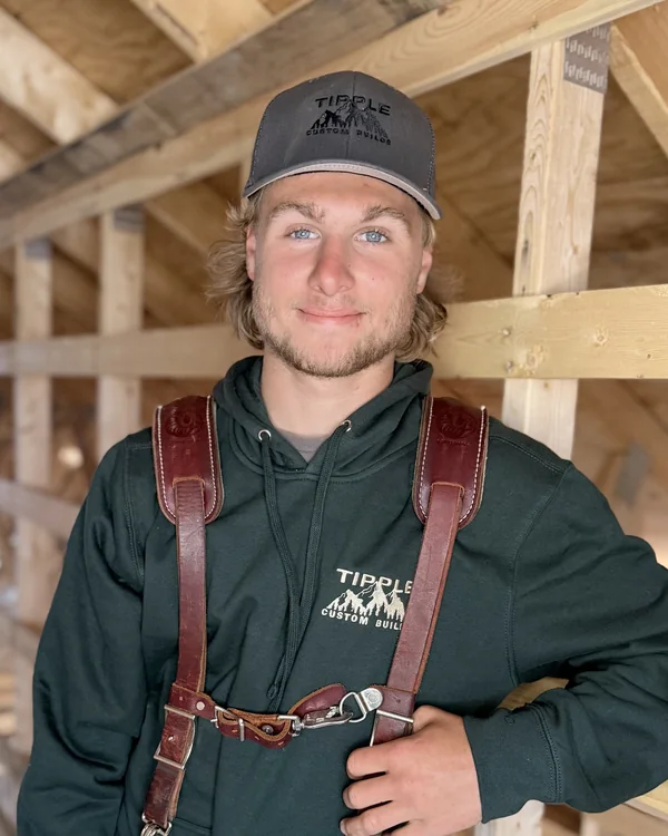 Connor Acker, in a framed attic in his company cap and leather tool-belt suspenders.