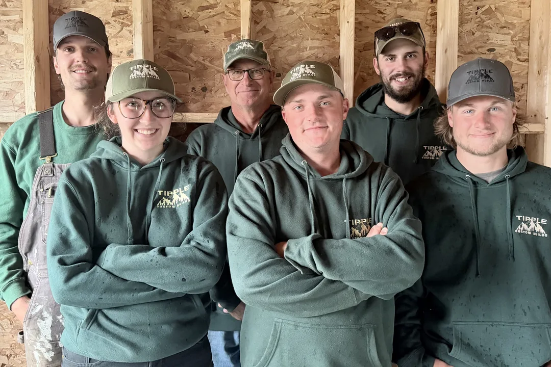 Six of the Tipple Custom Builds crew in matching green company hoodies and caps, standing together in front of a framed wall.