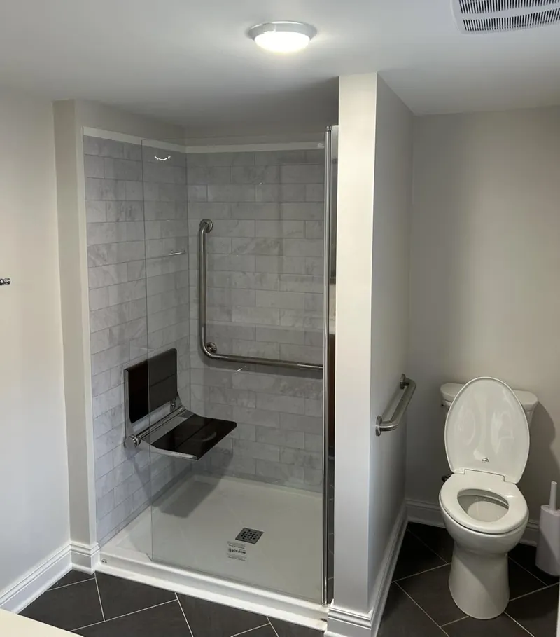 A curbless shower with a grab rail and a fold-down seat, tiled floor to ceiling.
