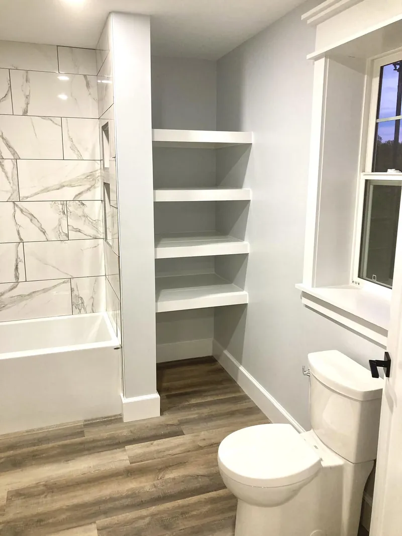 Built-in white shelving beside a tiled tub in a small bathroom.