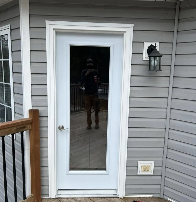 A new glazed entry door hung in a grey clapboard wall beside a timber rail.