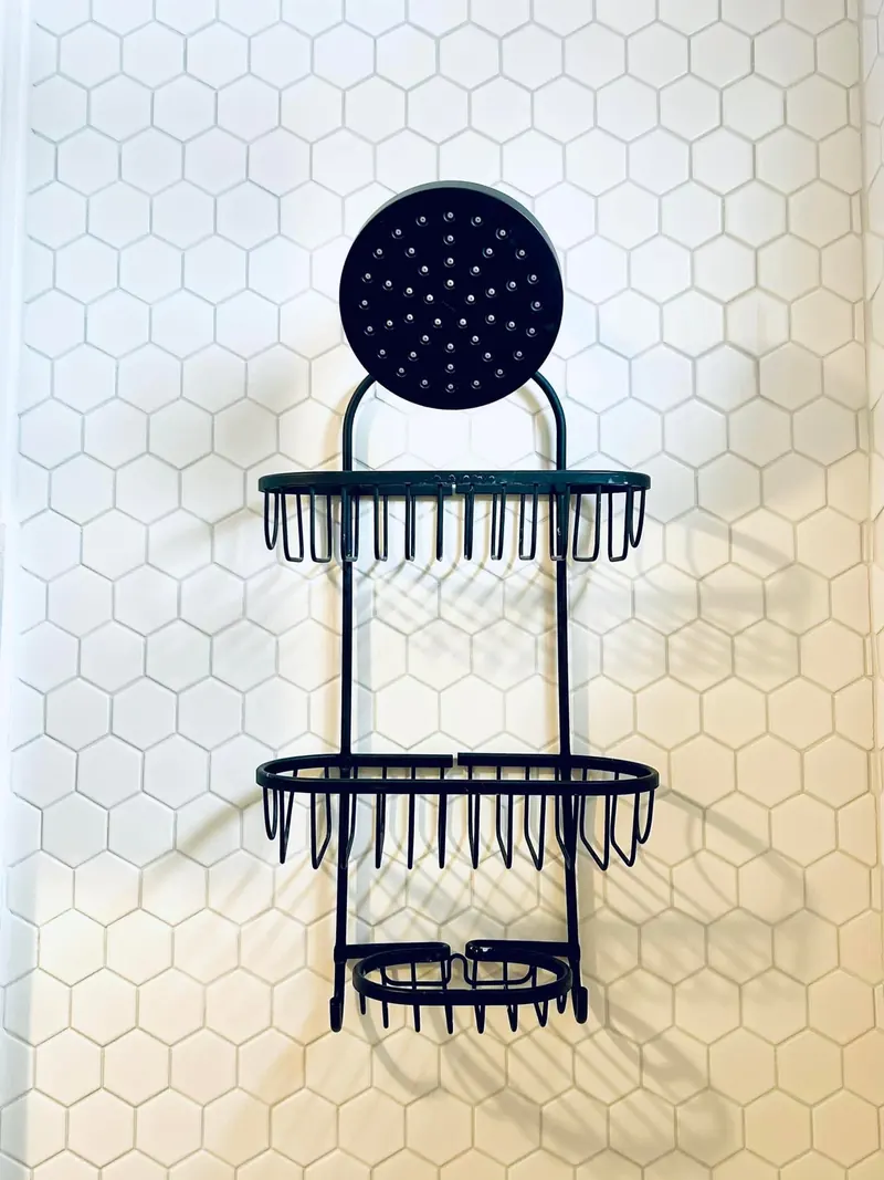 A shower wall in white hexagon tile with a black wire caddy hung on it.