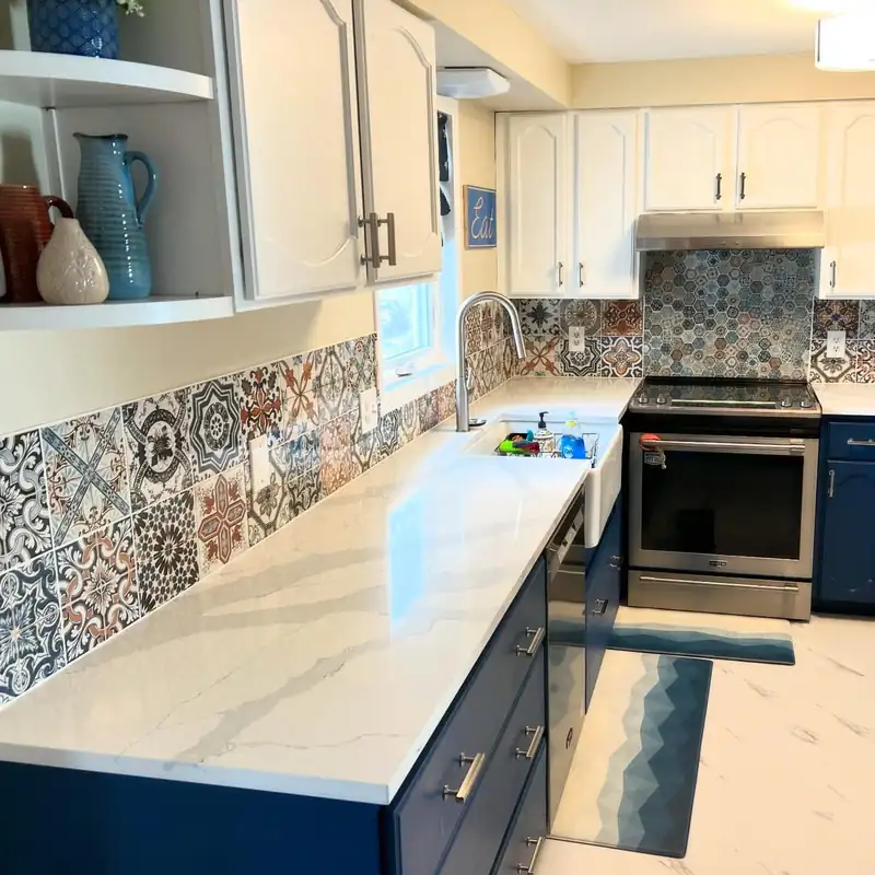 A kitchen with a navy island, stone counter and a patterned tile splash.