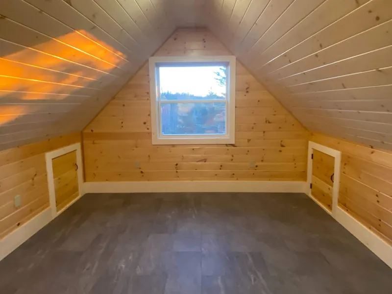 A dormer window framed and trimmed in a pine-lined loft.