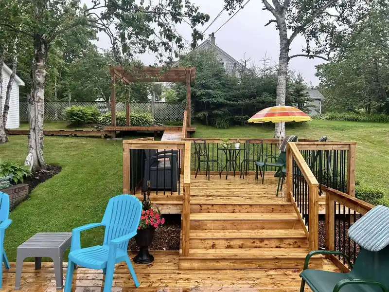 A large multi-level deck with a pergola, steps and patio furniture on a lawn.