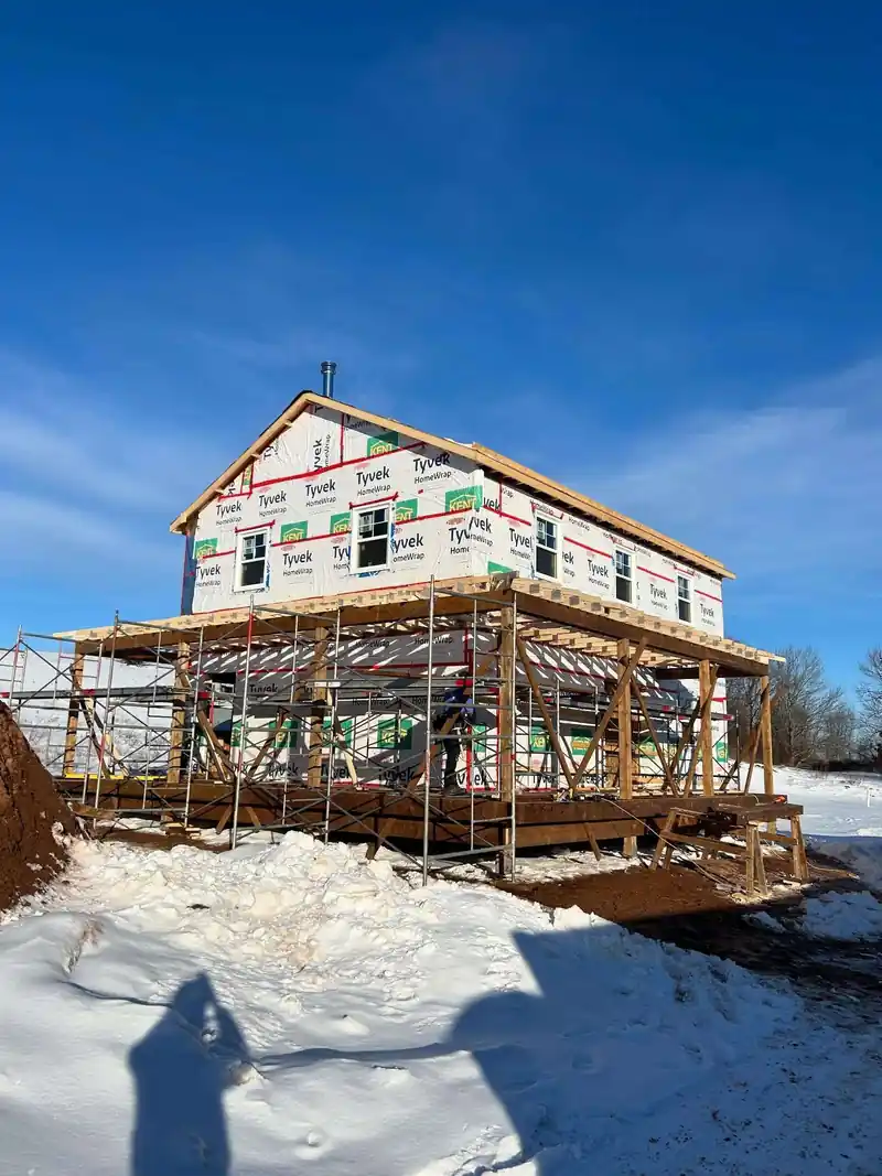 A two-storey house sheathed and wrapped with staging around it under a blue sky.