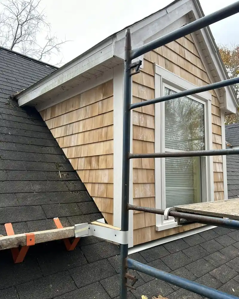 Cedar shingle courses running up to the rake of a dormer, staging in front.