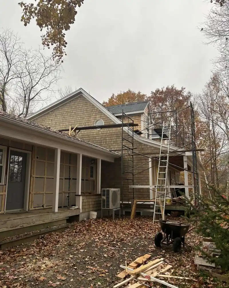 Cedar shingles part-way up a house wall, staging and a shingle pile alongside.