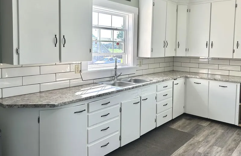A white shaker kitchen with a subway tile splash and a window over the sink.