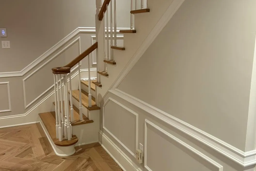 A rebuilt staircase with turned balusters and panelled wainscot, herringbone flooring at the foot of it.