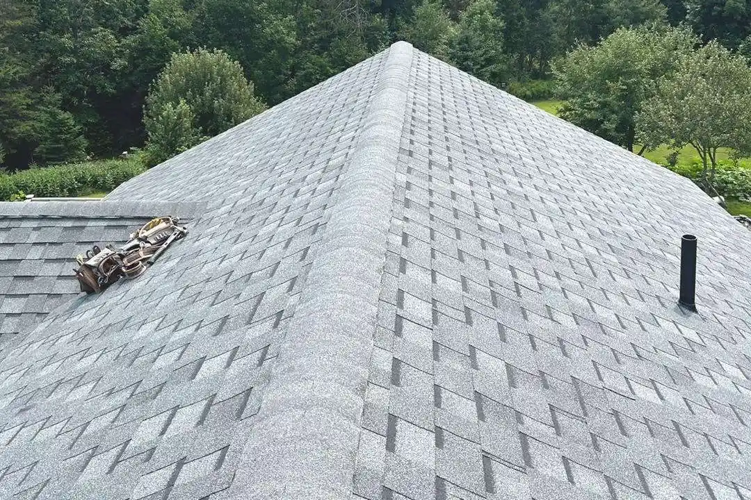 A newly shingled hip roof with the ridge cap run out, wooded hills beyond.