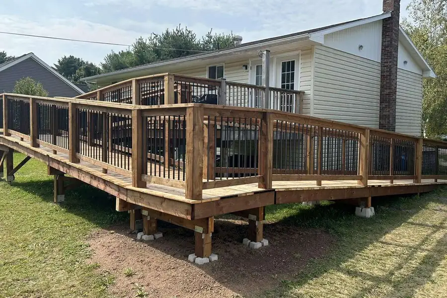 A cedar deck with black spindle railing wrapping the back of a bungalow.
