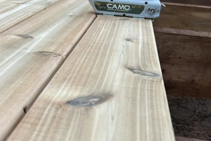 A Camo hidden-fastener tool sitting on a run of freshly laid cedar deck boards.