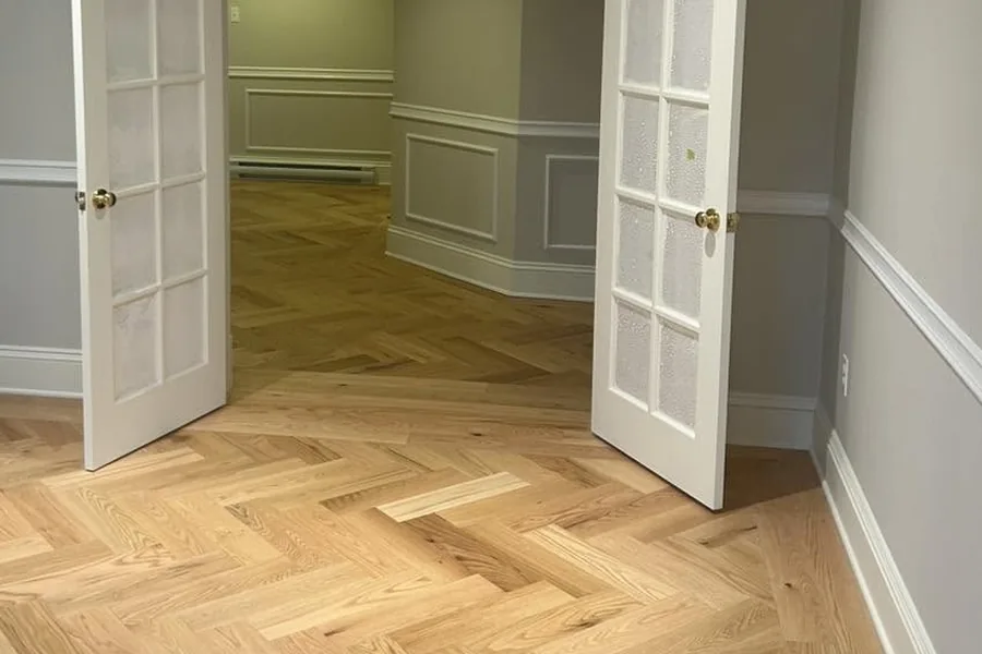 Red oak herringbone flooring running through a set of panelled french doors.