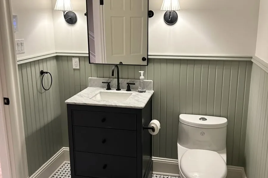 A finished powder room with basketweave floor tile, beadboard wainscot and a marble-topped vanity.